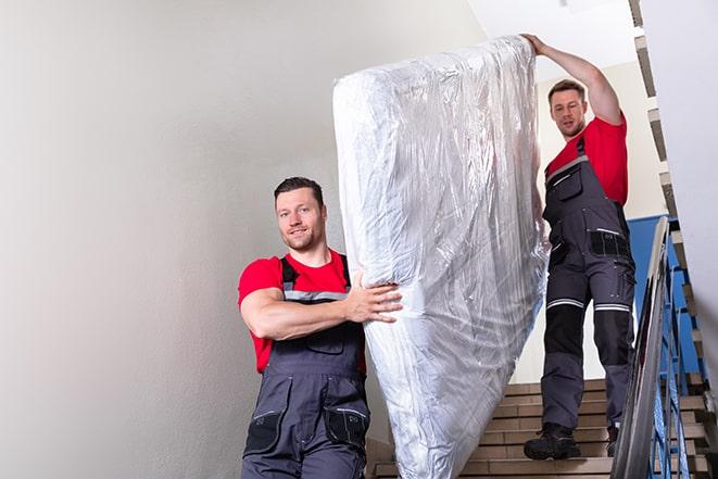 workers maneuvering a box spring through a narrow hallway in Bonita